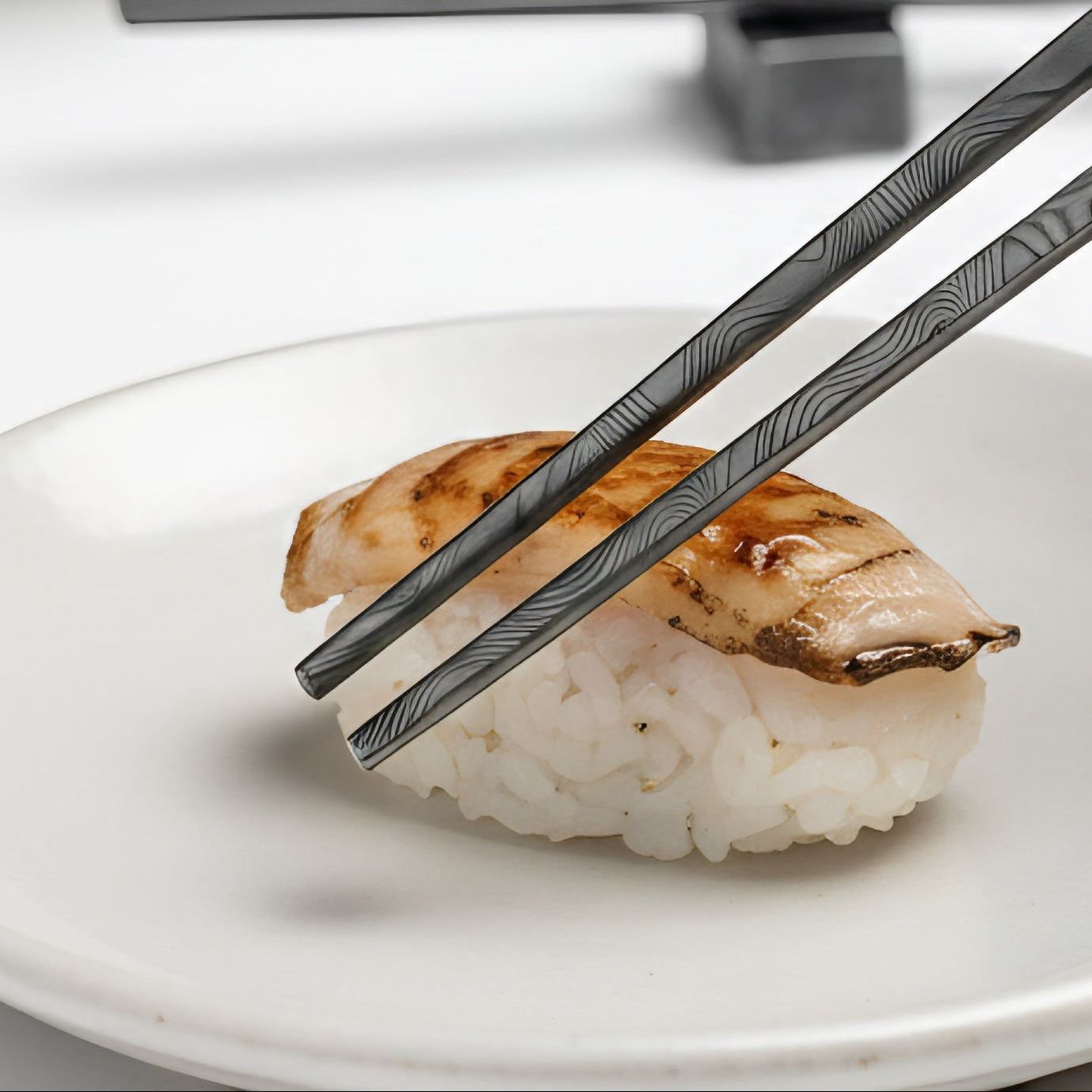 Person using chopsticks to pick up sushi from a plate with a bowl in the background.