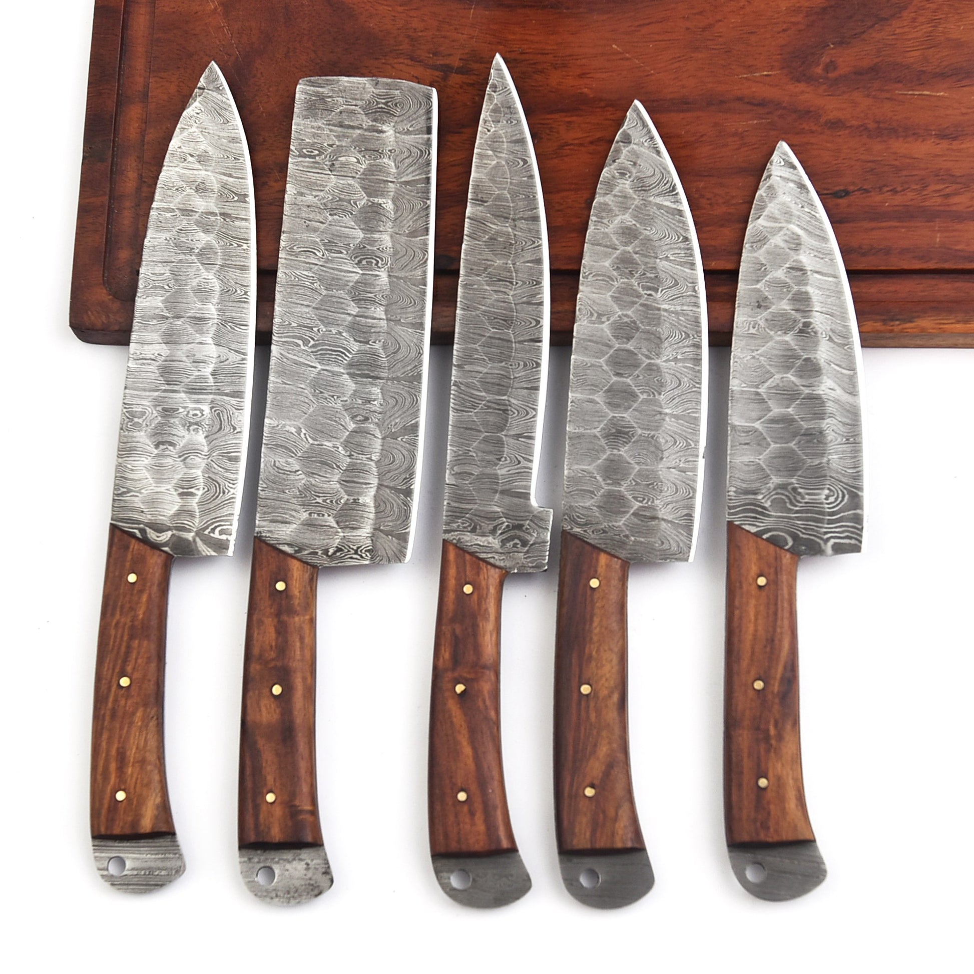 Set of five Damascus steel kitchen knives with wooden handles on a wooden surface.