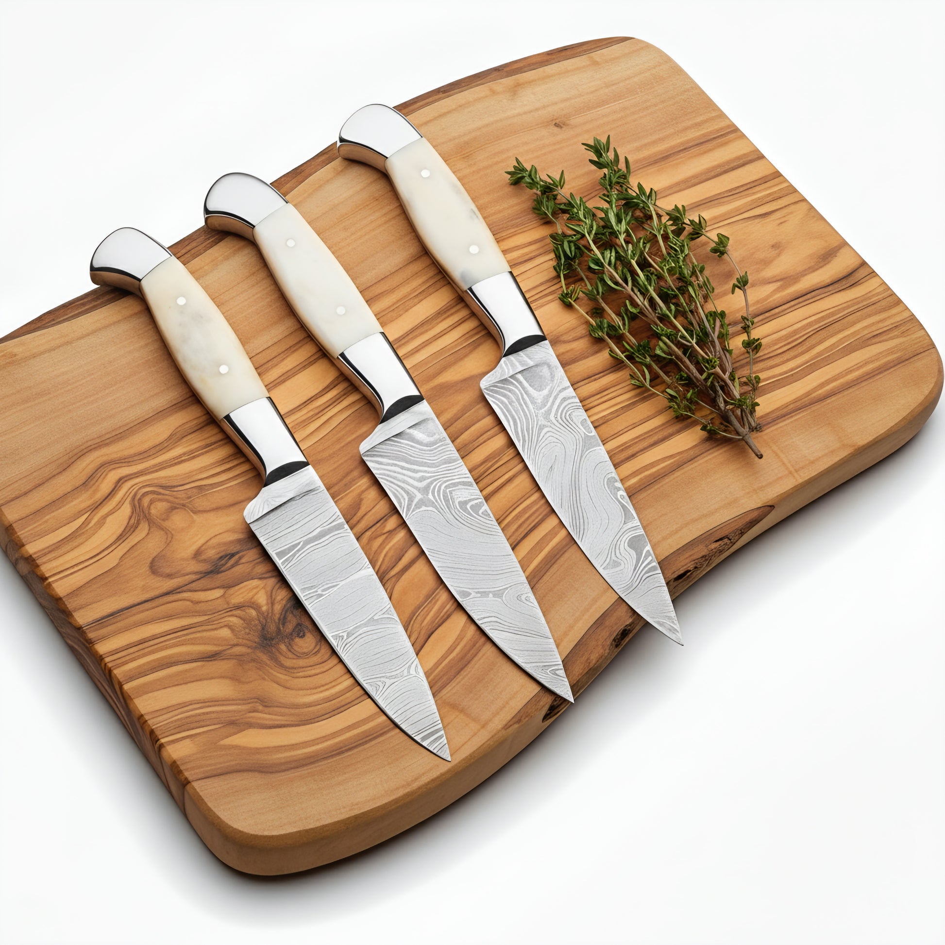 Set of four knives with white handles on a wooden cutting board with herbs.