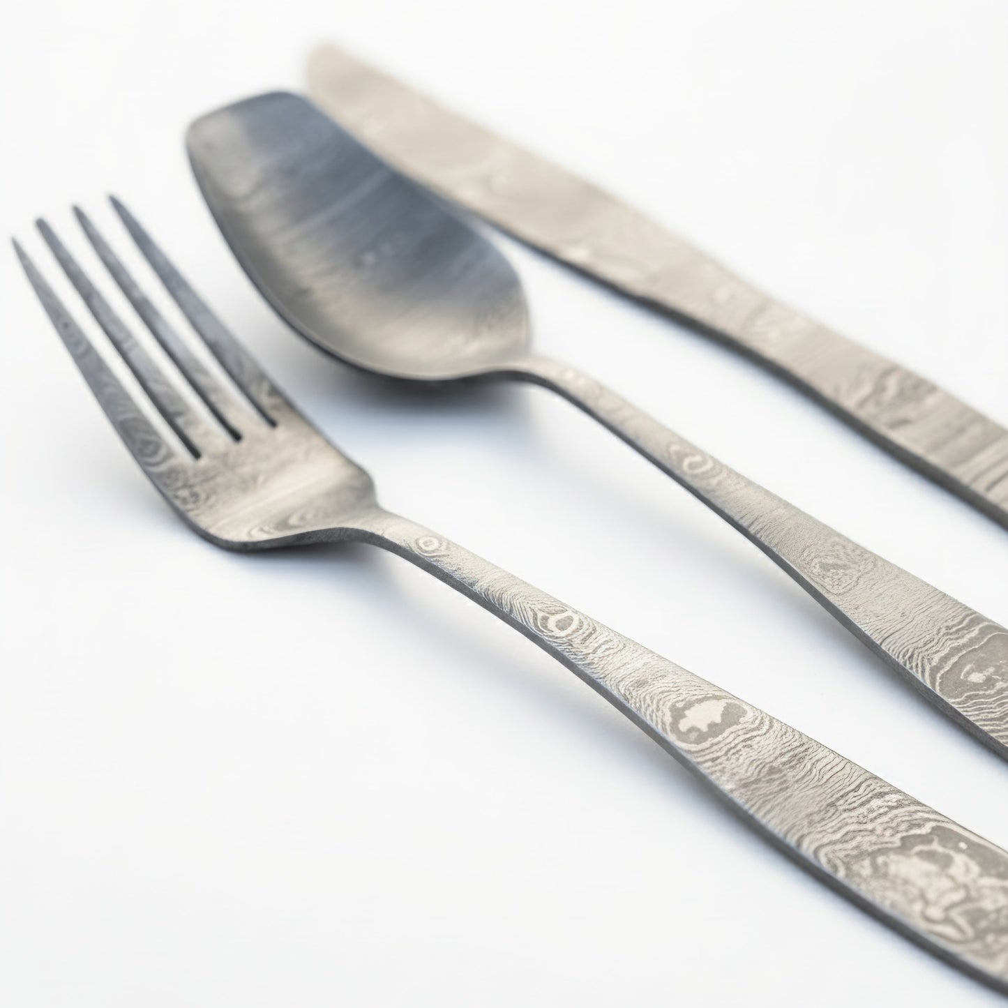 Set of silver cutlery including a fork, knife, and spoon on a white background Damascus cutlery set