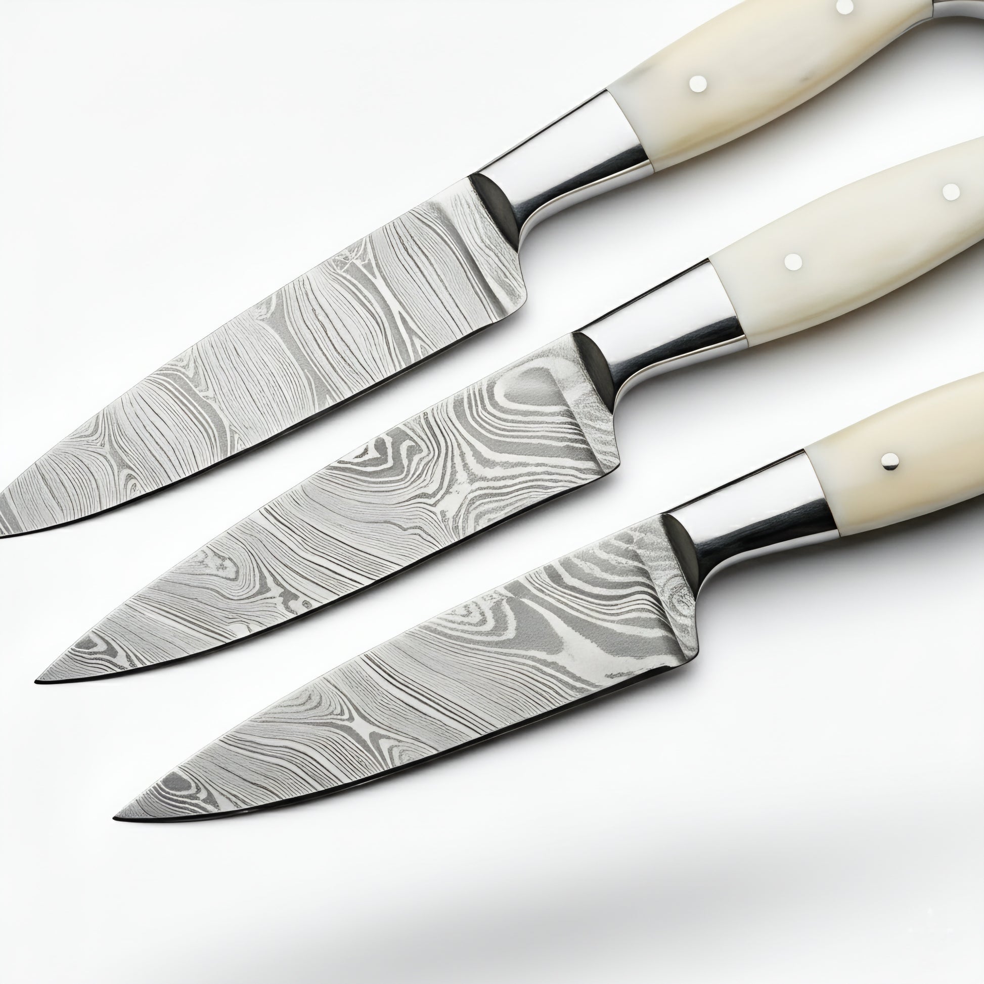 Set of three knives with damascus steel blades and white handles on a white background