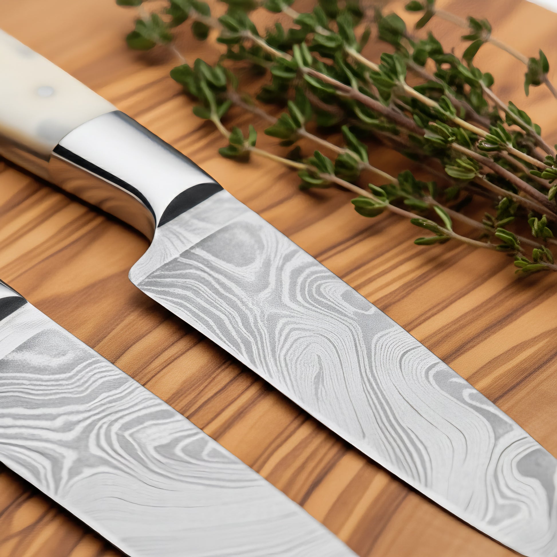Two Damascus steel knives on a wooden surface with fresh herbs.