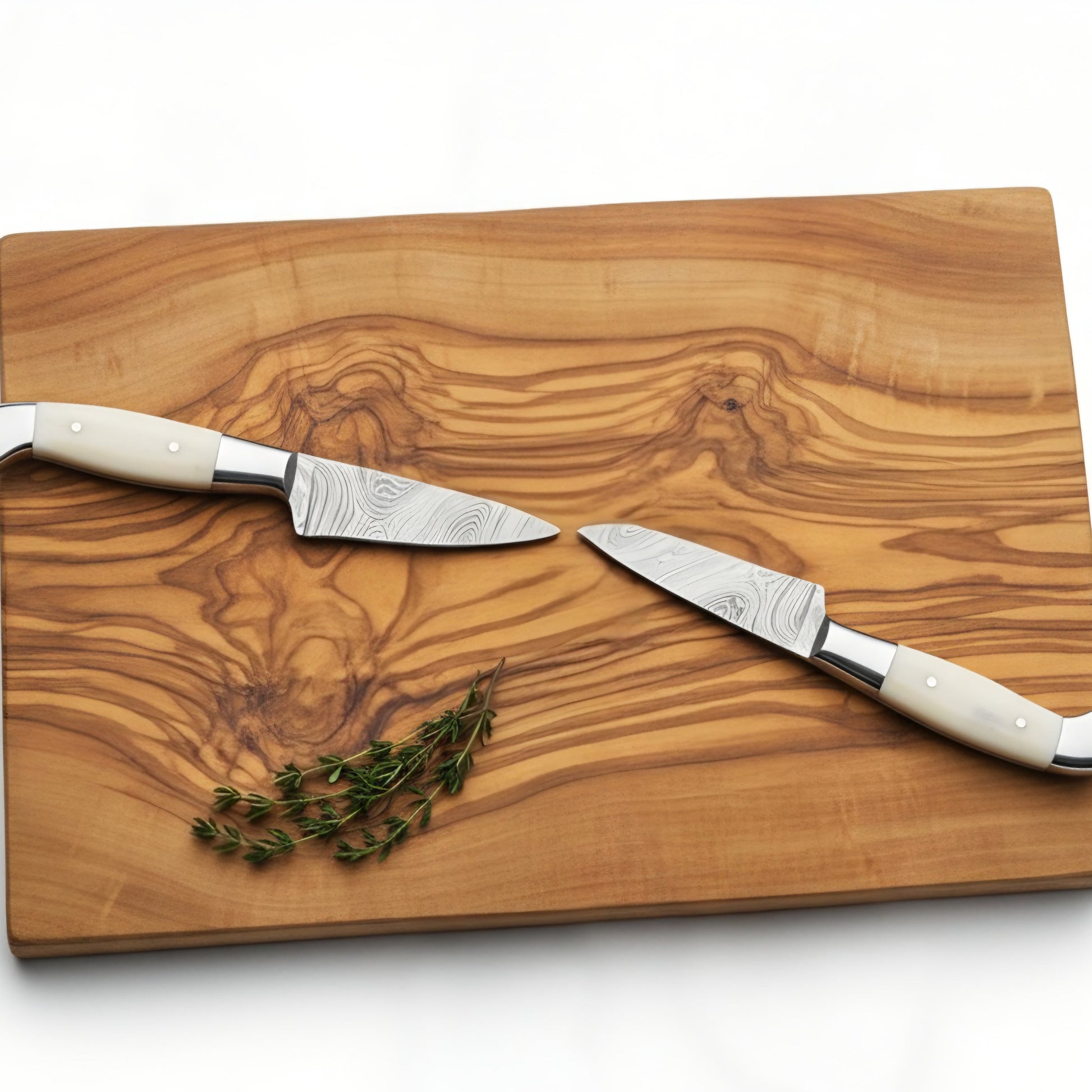 Wooden cutting board with two knives and a sprig of thyme on a white background