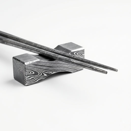 Decorative metal chopstick rest with intricate patterns on a white background