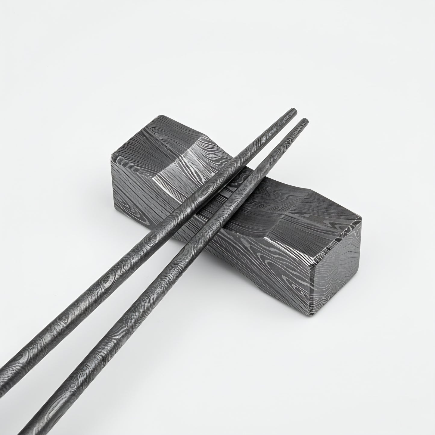 Black and silver patterned chopsticks on a matching black and silver box against a white background