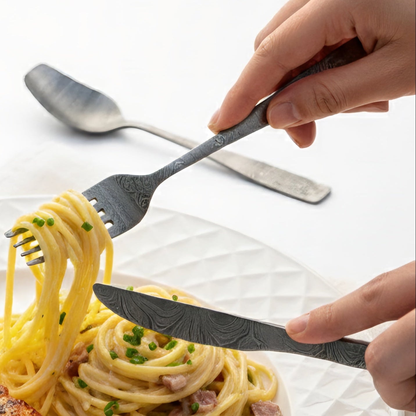 Fork and knife with decorative patterns over a plate of pasta. Damascus cutlery set