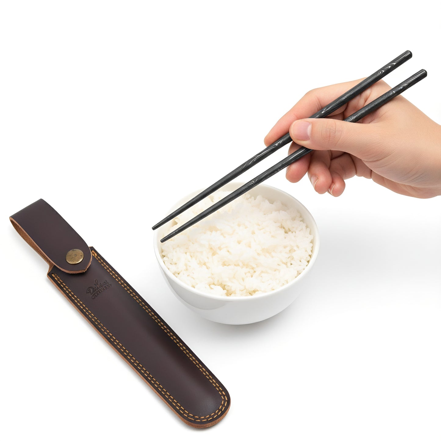 Hand holding black chopsticks over a bowl of rice with a brown leather case on a white background