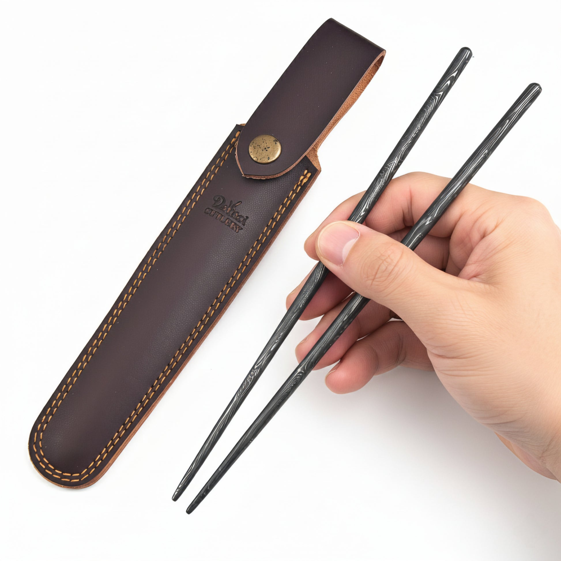 Hand holding black metal chopsticks with a brown leather case on a white background
