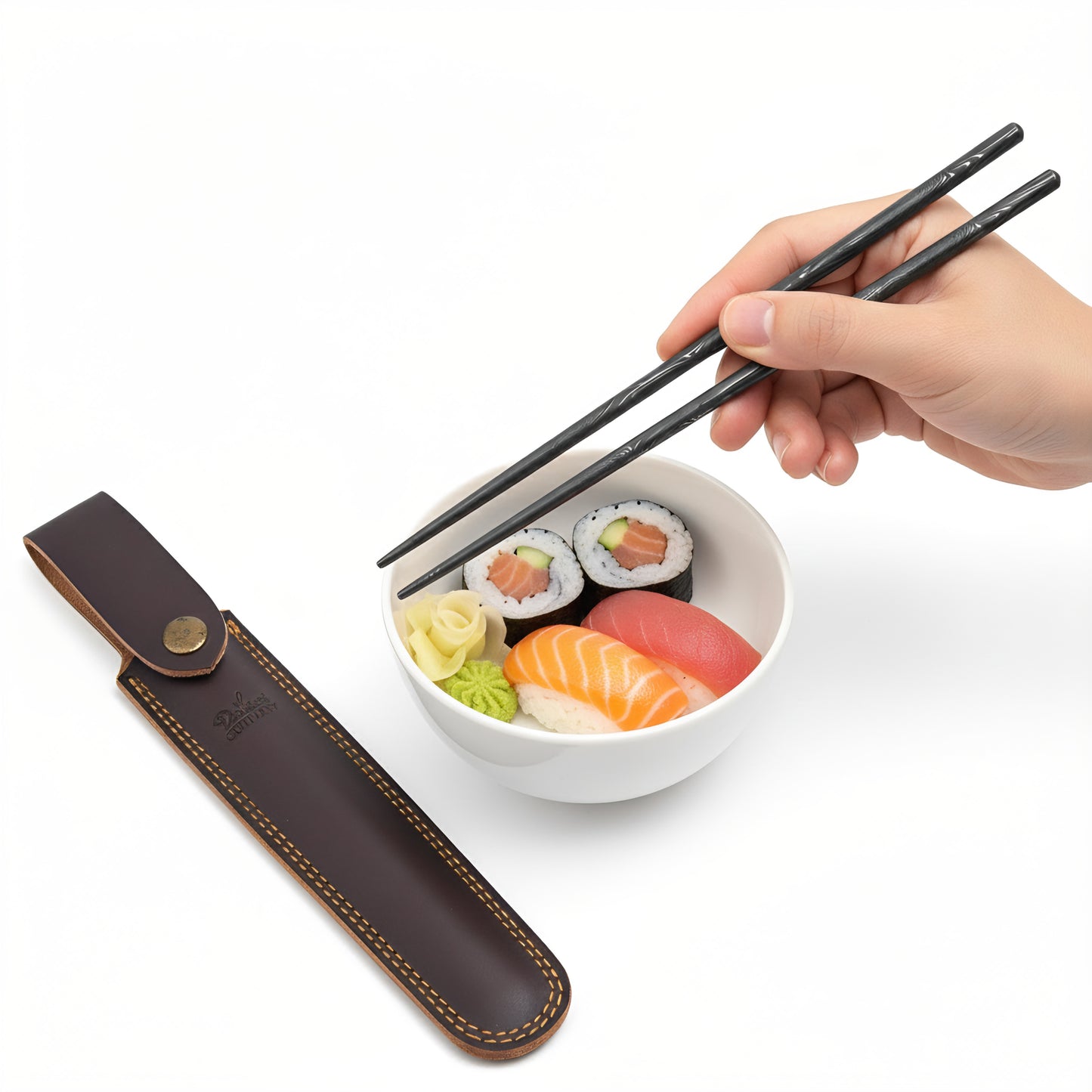 Hand holding chopsticks over a bowl of sushi with a brown leather case on a white background
