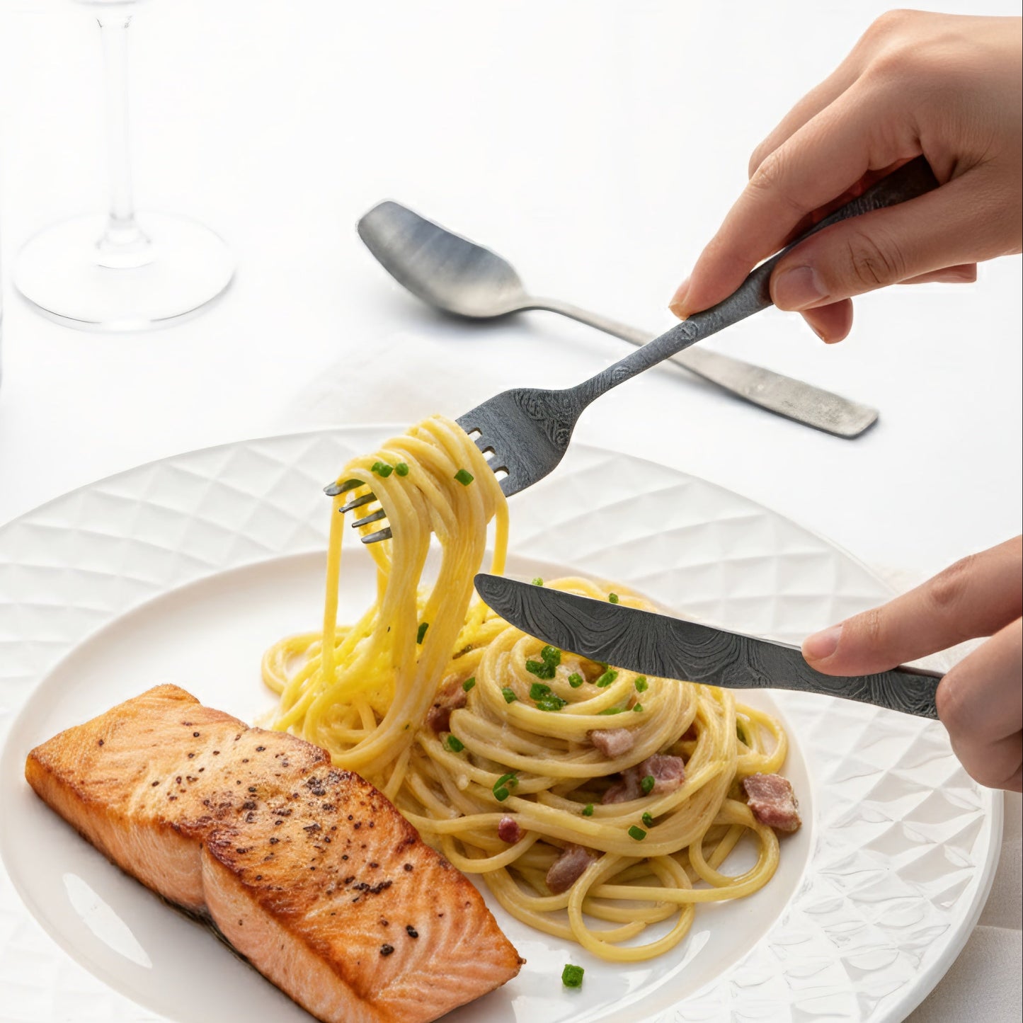 Plate of pasta with salmon being eaten by a person on a white table Damascus cutlery set