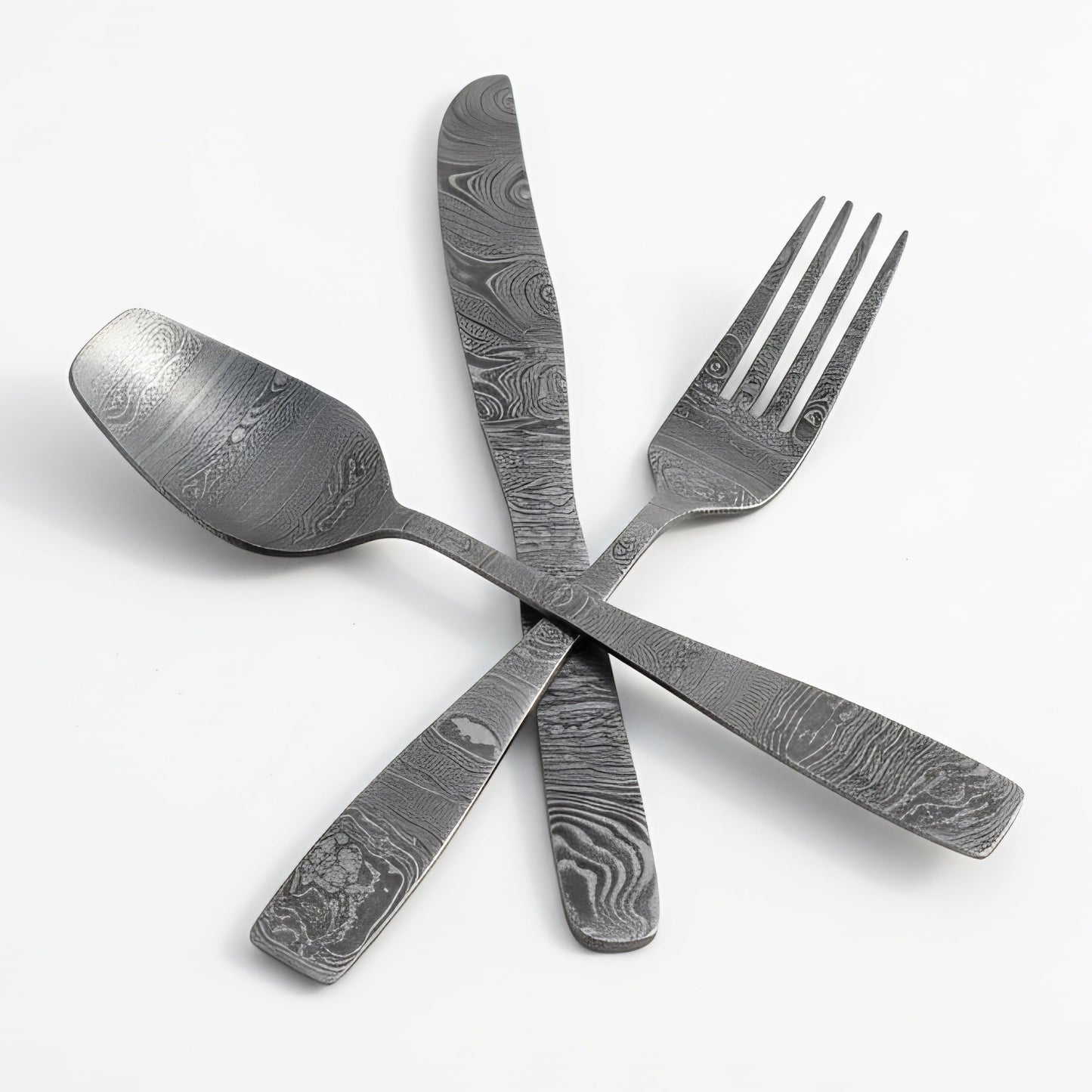Set of damascus steel cutlery including a spoon, knife, and fork on a white background Damascus cutlery set