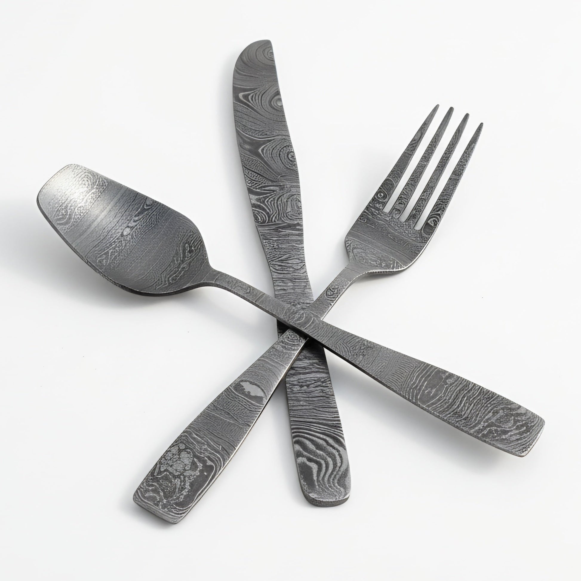 Set of damascus steel cutlery including a spoon, knife, and fork on a white background Damascus cutlery set