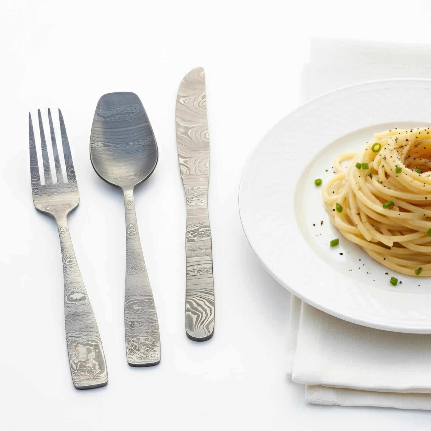 Silver cutlery set with a plate of pasta on a white background Damascus cutlery set