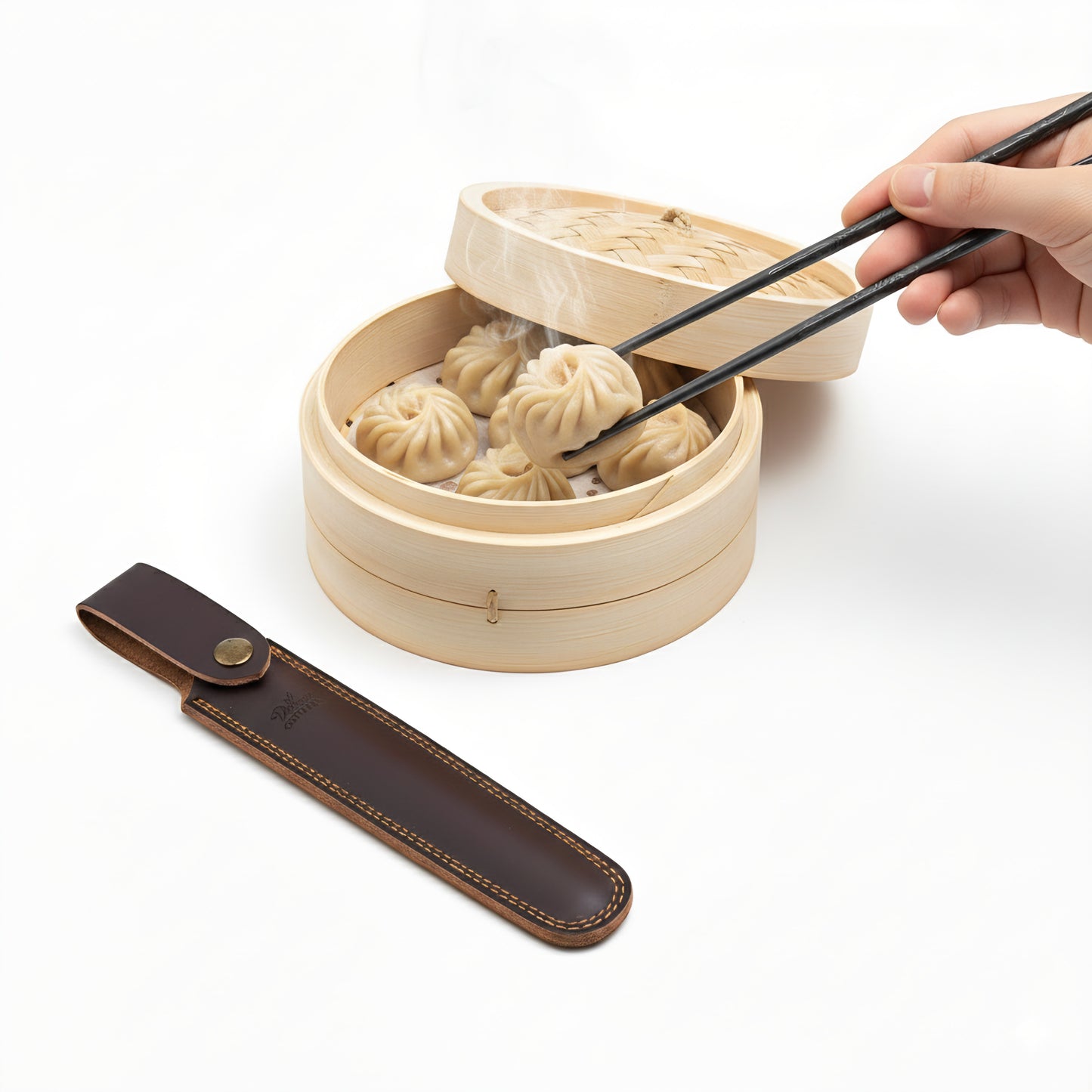 Wooden steamer with dumplings and a hand using chopsticks to pick up a dumpling on a white background.
